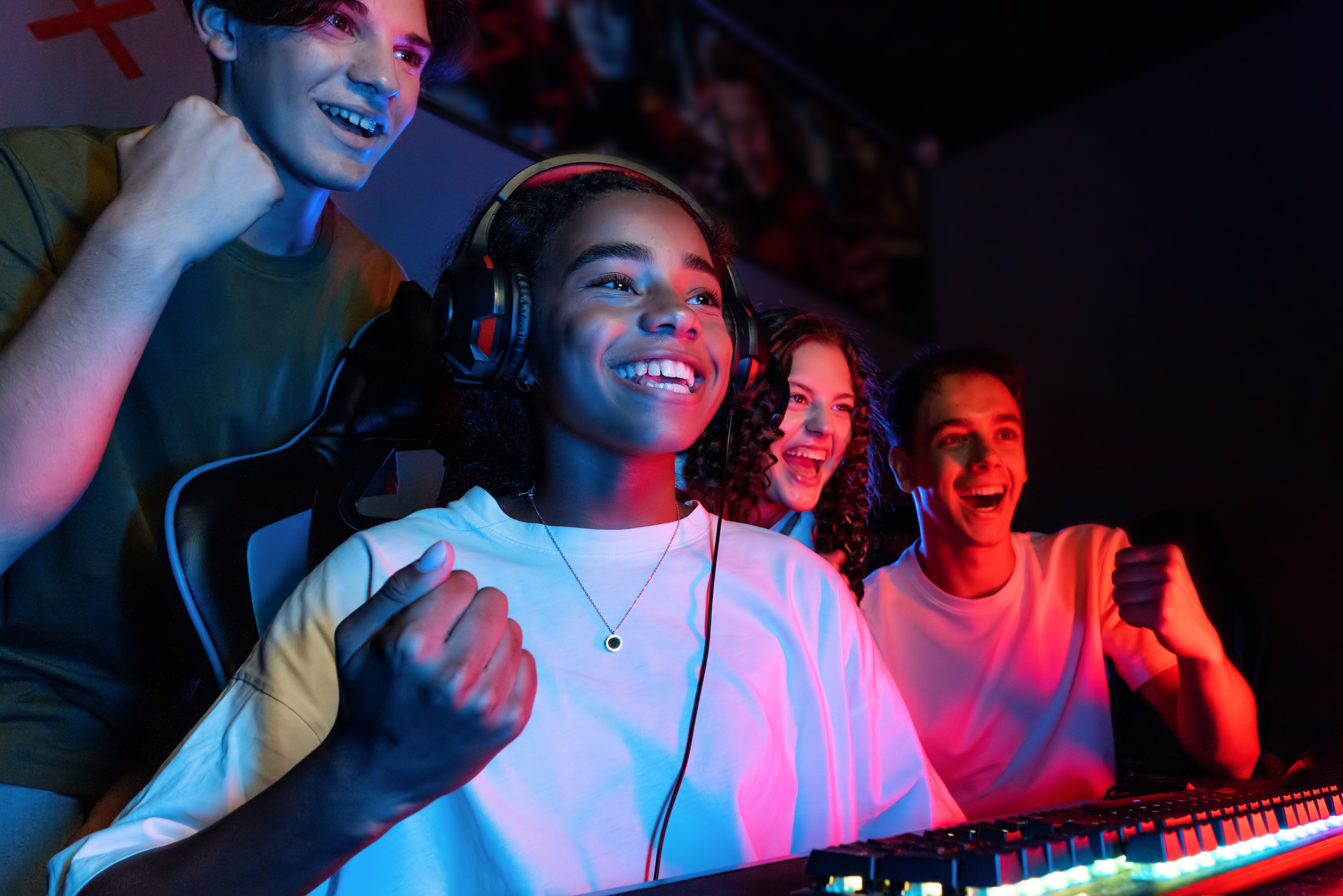 Imagem contendo vários adolescentes, em frente a um monitor, comemorando a vitória no jogo de uma das garotas.
