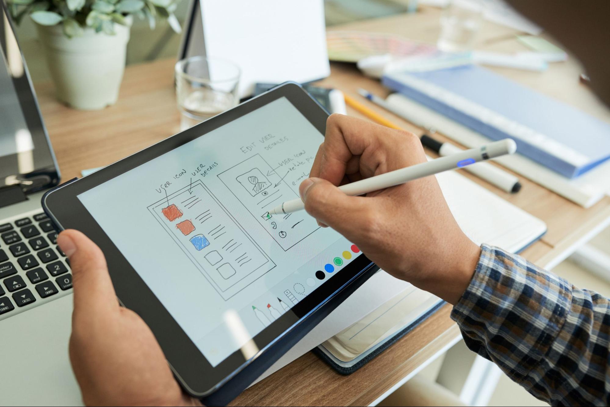 Imagem em que vemos uma pessoa com uma caneta na mão fazendo um projeto em um tablet.