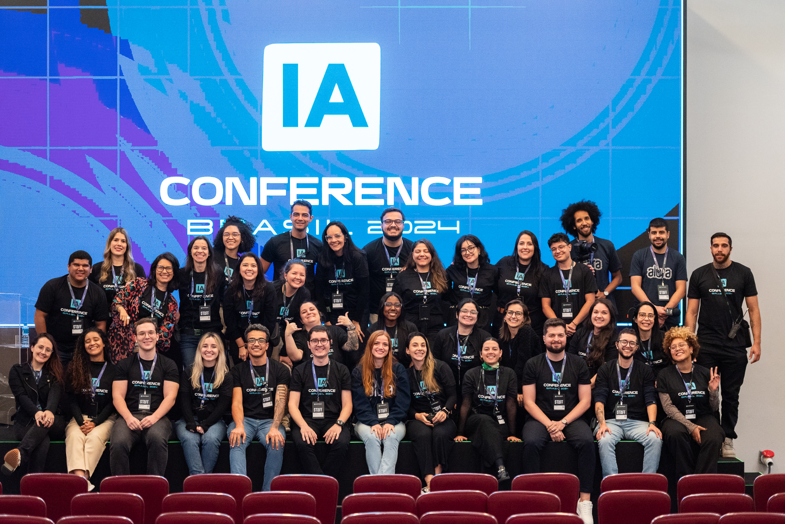 Na fotografia, estão todas as pessoas que participaram da organização do IA Conference Brasil. Todas as pessoas estão de camiseta preta escrito “IA Conference Brasil 2024” em verde e branco