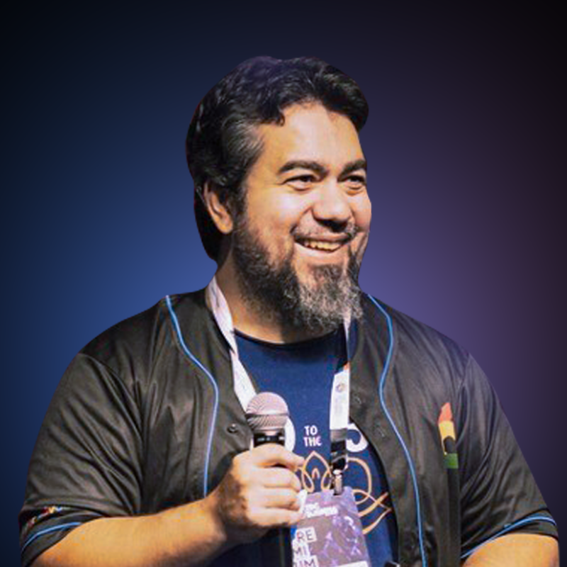 Imagem de Luciano Martins, Developer Advocate, Google IA. Luciano está com uma camiseta azul e uma jaqueta preta, um microfone está sendo segurado na sua mão direita e o fundo é um gradiente roxo.