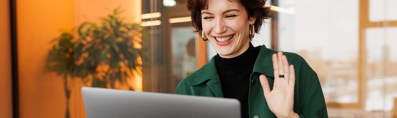 mulher sorrindo acenando para um notebook em um ambiente de trabalho representando a geração Z no mercado de trabalho