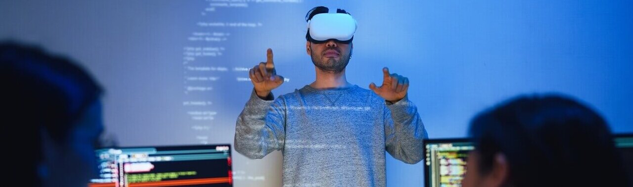 um homem utilizando um óculos de realidade virtual em frente a pessoas desenvolvendo códigos, representando a importância das mad skills nas empresas